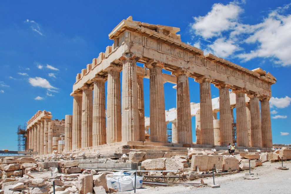 The Parthenon, an iconic ancient temple with Doric columns, stands atop the Acropolis in Athens under a bright blue sky.