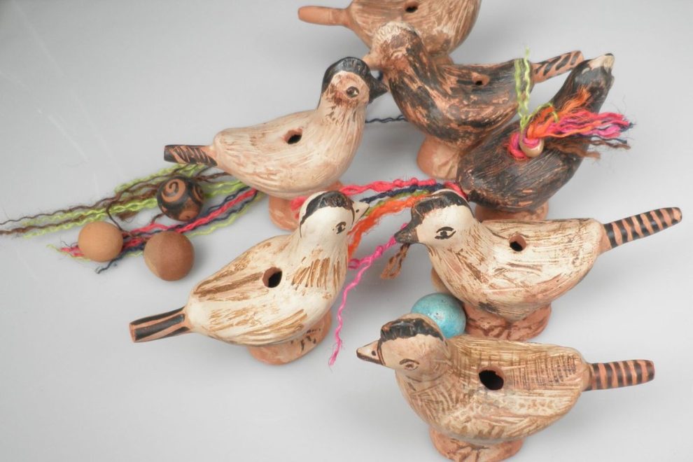 A set of bird-shaped clay whistles from ancient Greece, decorated with simple patterns and colorful strings, accompanied by small balls.