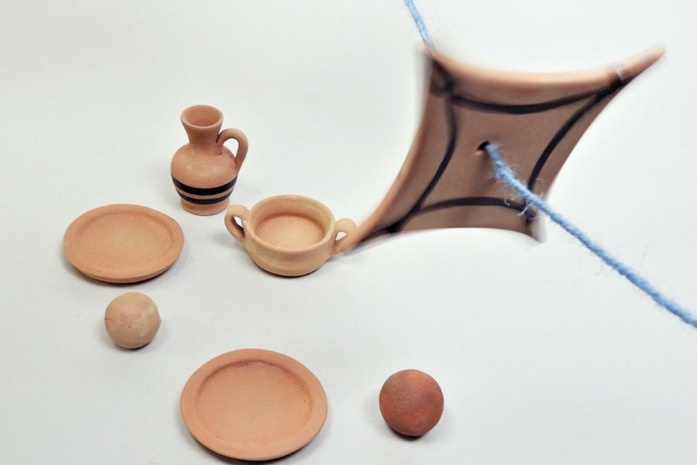 A collection of ancient Greek-inspired clay toys, including miniature plates, a jug, a bowl, small balls, and a spinning toy attached to a string.