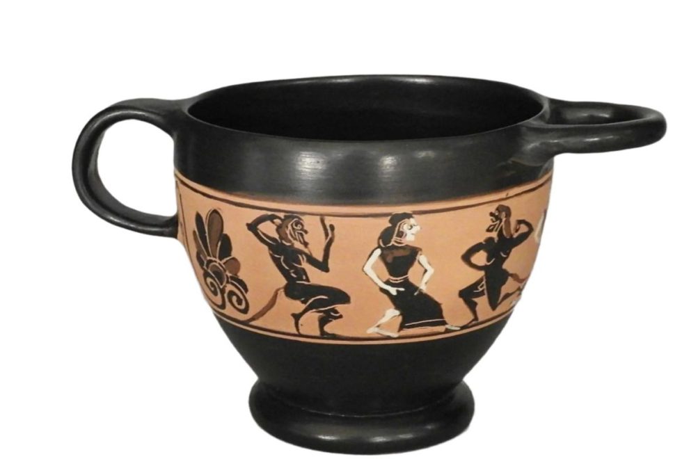 An ancient Greek ceramic cup with black-figure artwork depicting dancing figures and decorative floral motifs.