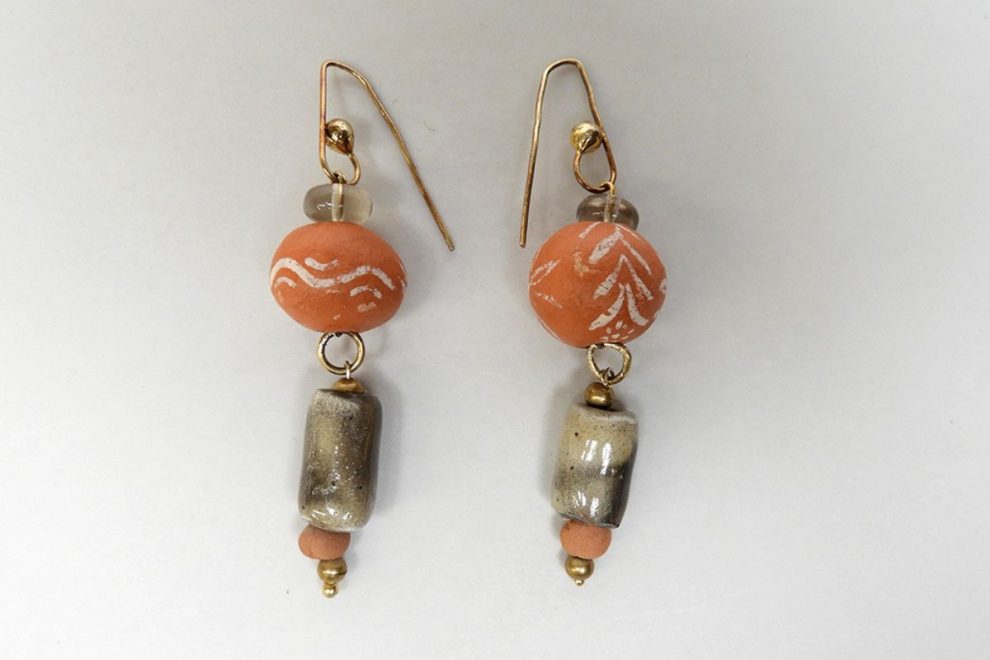 A pair of handmade terracotta-colored earrings in an Ancient Greek style, featuring simple white patterns and gold hooks.