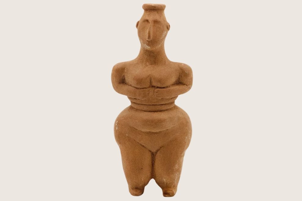 A terracotta female figure with a rounded silhouette, crafted in an Ancient Greek style.