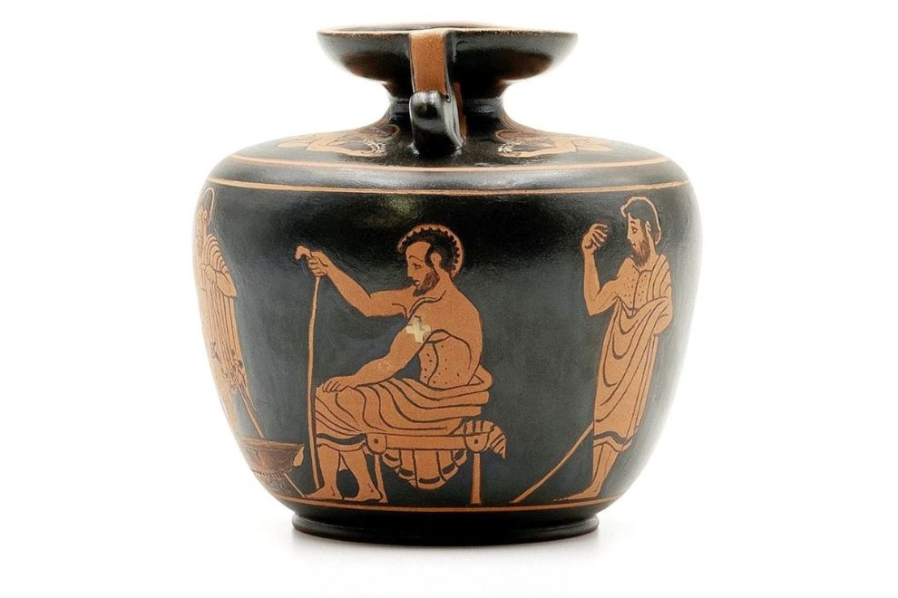 A Greek red-figure aryballos depicting a medical scene with Erotes. The vase features detailed figures, including a seated bearded man holding a staff and other standing figures engaged in interaction. The black background contrasts with the reddish-orange illustrations, characteristic of ancient Greek pottery.