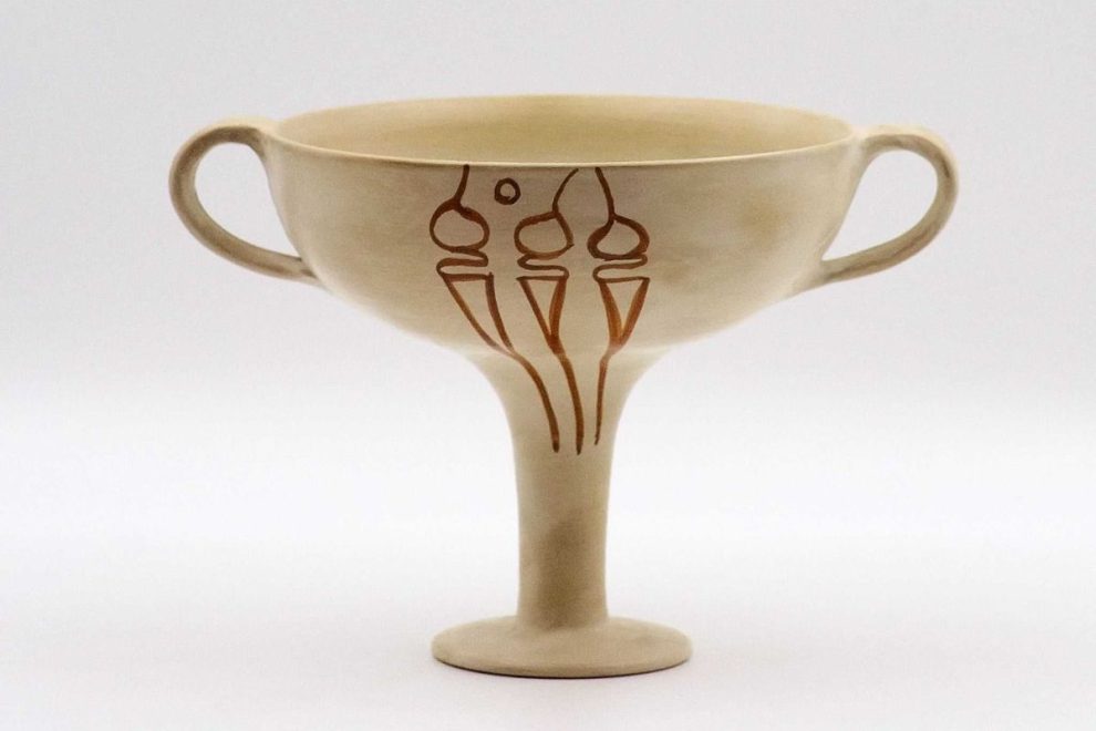 A Mycenaean Kylix with a tall stem and two handles, featuring a simple decorative motif on its surface. The light-colored pottery has a minimalistic design, characteristic of Mycenaean ceramics_old greek pottery