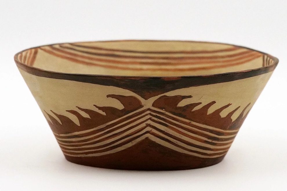 A Sesklo bowl featuring a flame-like decorative pattern in red and brown tones on a light background. The design is symmetrical, with curved and linear elements.